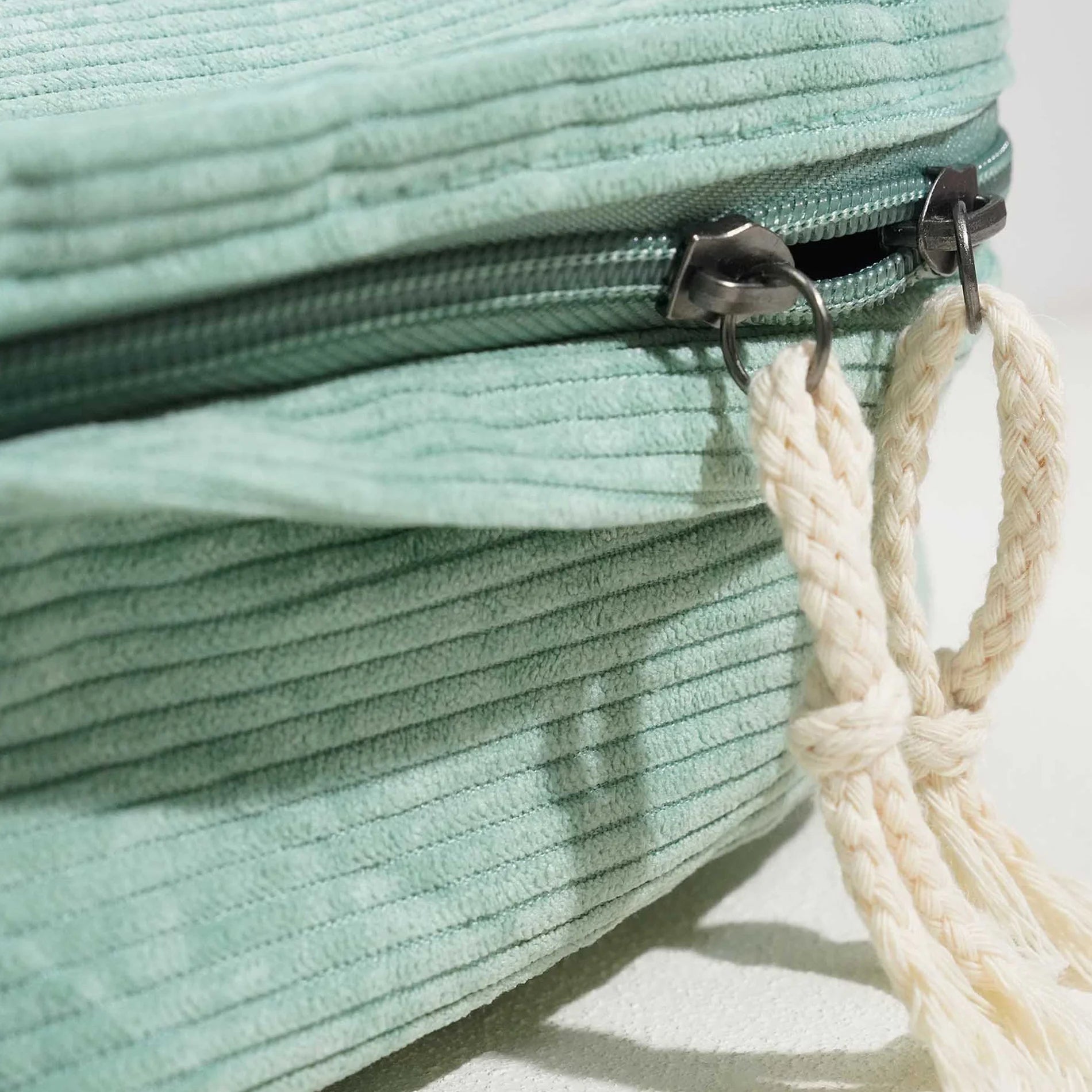 Close-up of a teal textured bag with a metal zipper and beige rope handle.