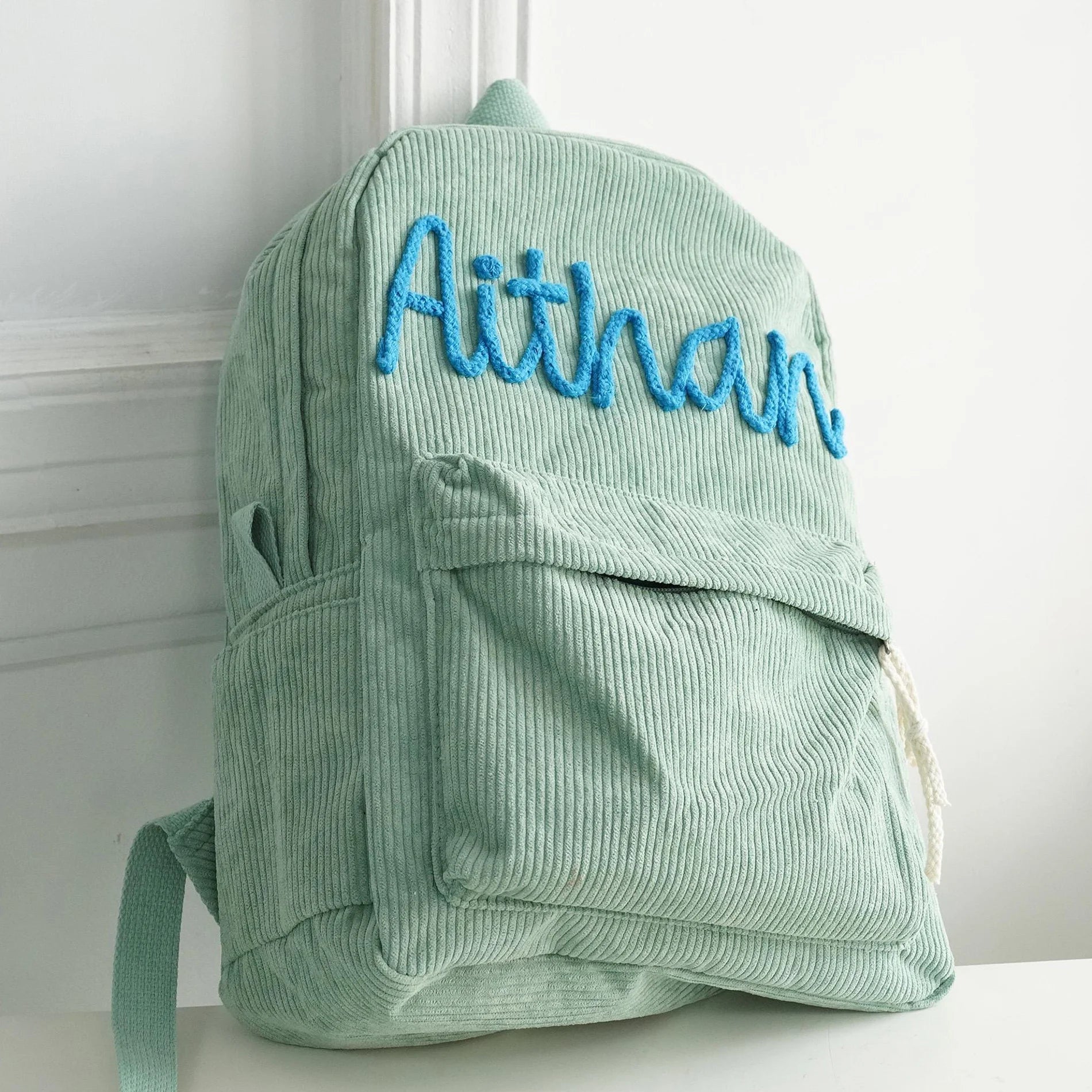 Green corduroy backpack with 'Aithan' embroidered on it against a white background